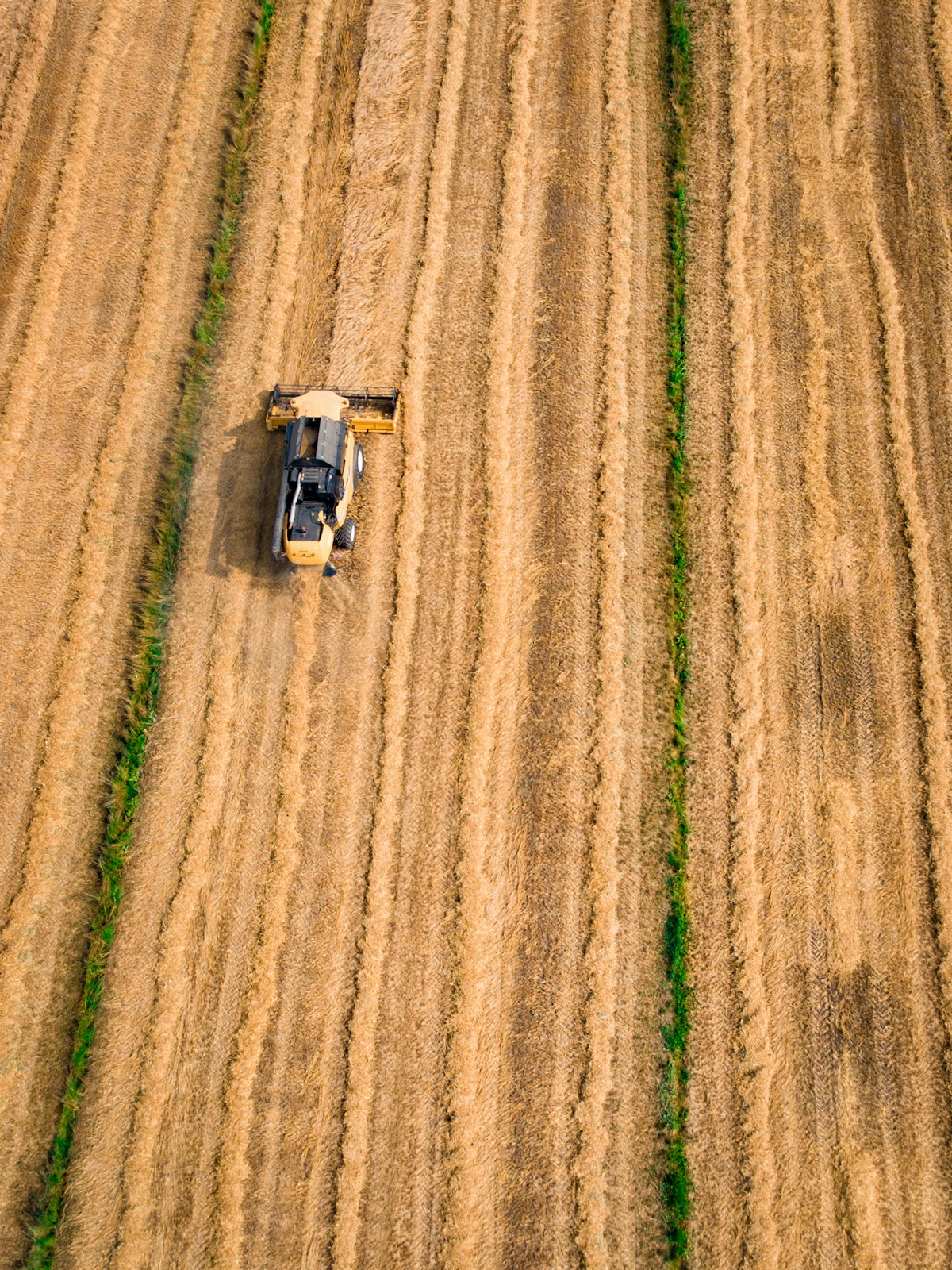 Vista aérea de máquina agrícola amarela em campo arado marrom com padrão geométrico